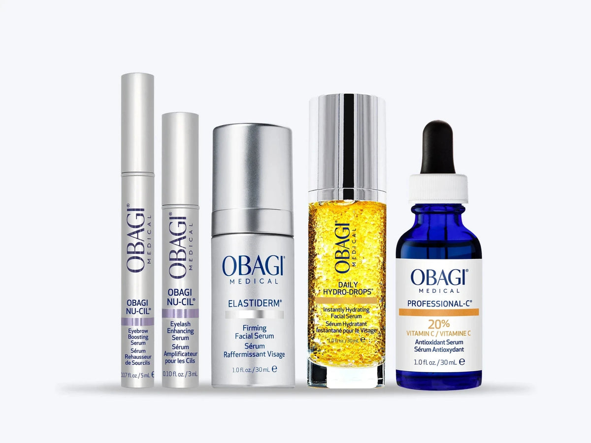 A five-piece Obagi Medical skincare set arranged in a row against a light gray background. The set includes silver and white bottles and tubes, a clear bottle filled with golden-yellow serum, and a dark blue dropper bottle with a black cap.